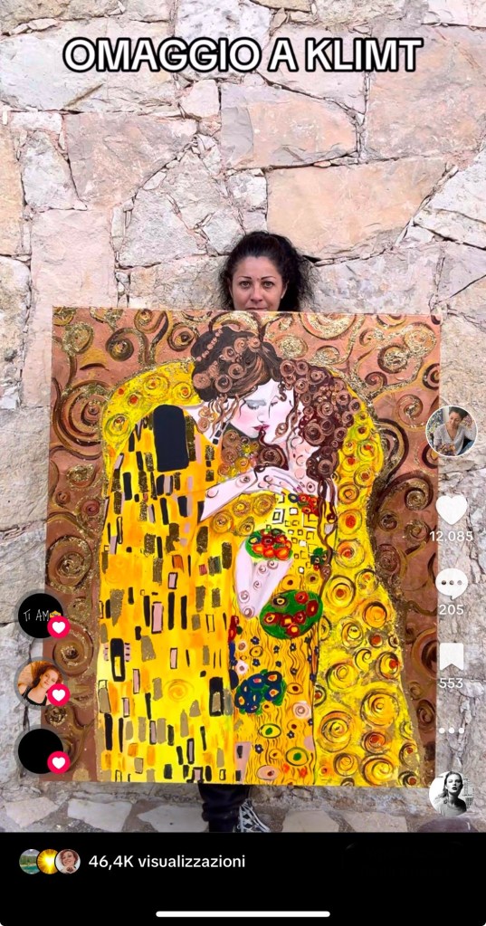 Immagine di Claudia Ottone che mostra il suo quadro di grandi dimensioni in una schermata del video di tik tok. Il quadro raffigura una rivisitazione del quadro il bacio di klimt, in versione Lgbtq+ di due donne che si baciano. I colori predominanti sono quelli di Klimt con un gusto più contemporaneo.